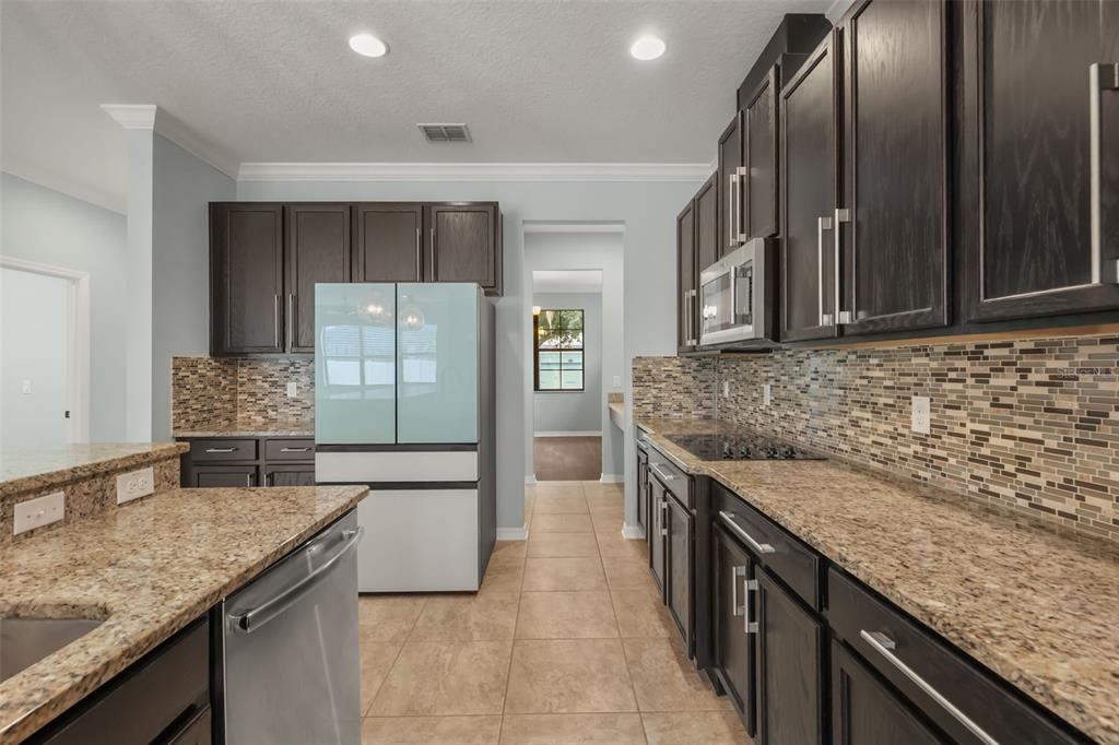 A kitchen features dark wood cabinets, granite countertops, a mosaic tile backsplash, and tile flooring — 5729 RUE GALILEE LANE, SANFORD, FL