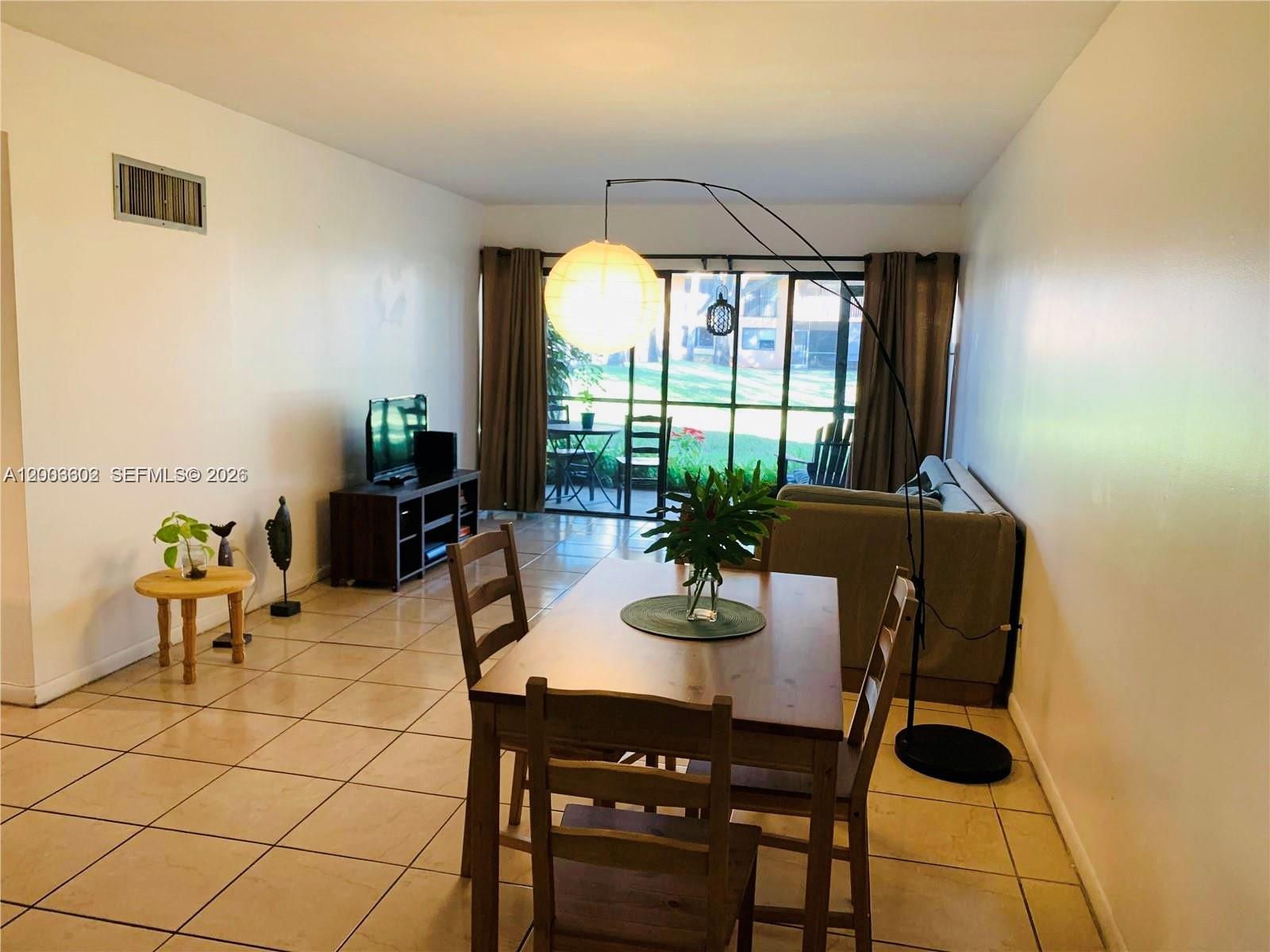 A dining area with a wooden table and chairs sits in front of a sliding door — 5855 Washington St # 90, Hollywood FL 33023, HOLLYWOOD, FL