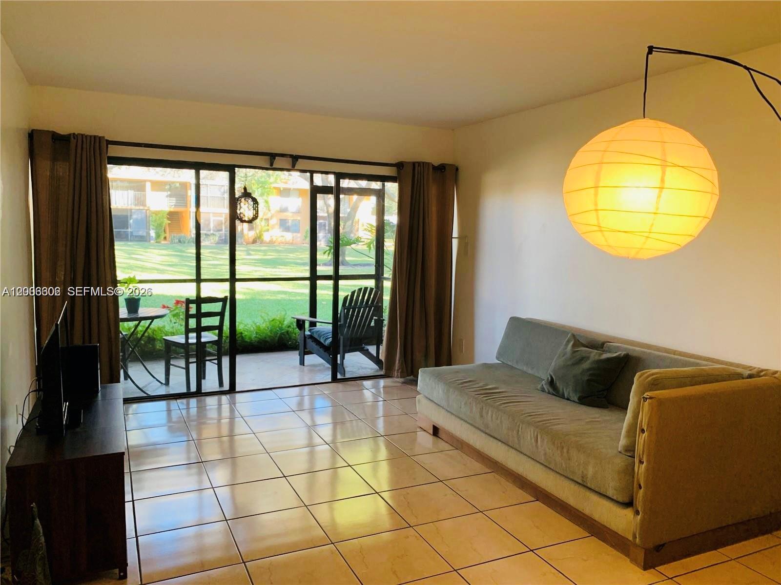 A living room features tile floors, a sofa, a floor lamp, and a sliding glass door — 5855 Washington St # 90, Hollywood FL 33023, HOLLYWOOD, FL