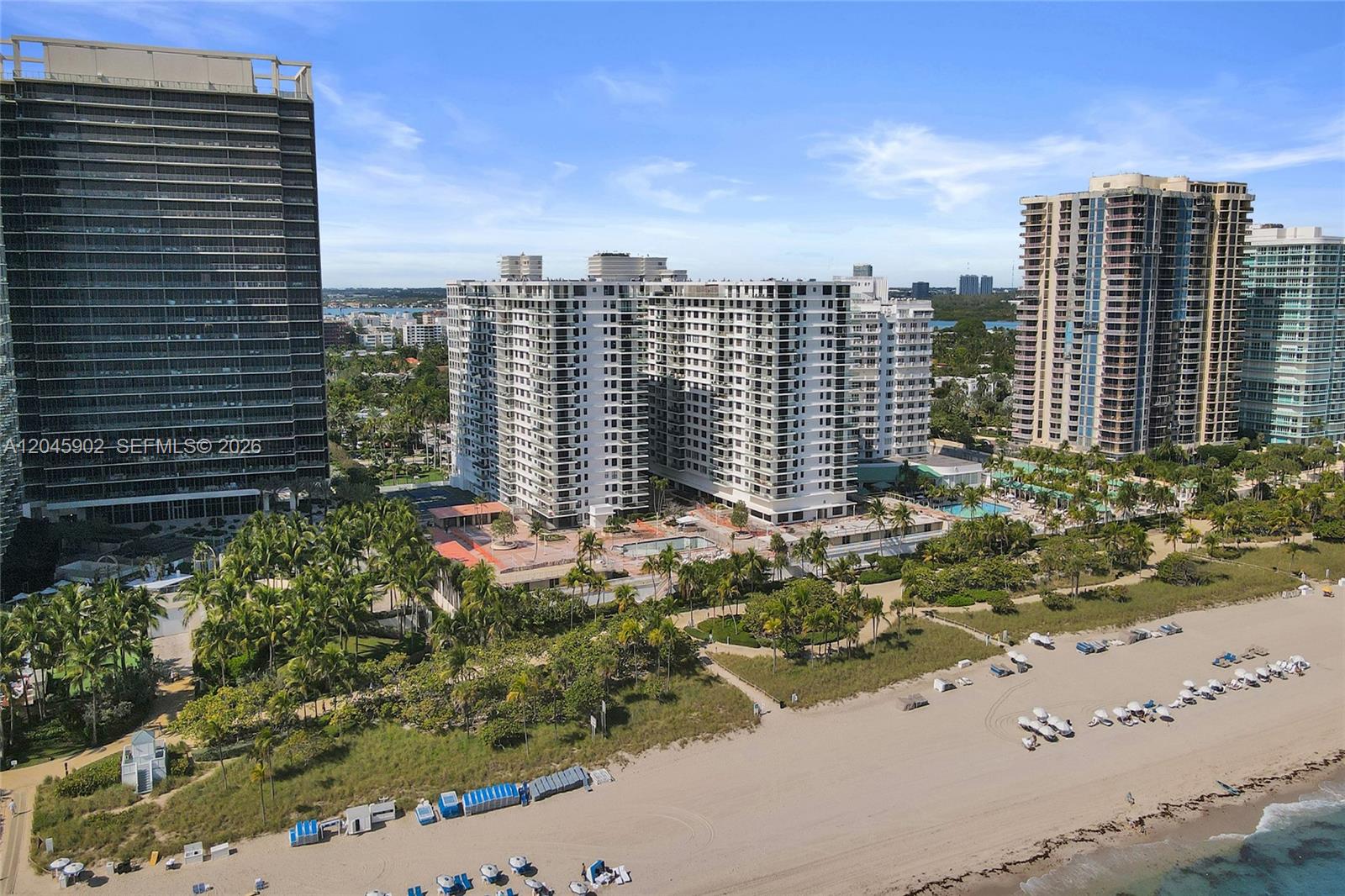 An aerial view shows high-rise residential buildings situated along a sandy beach with palm trees — 9801 Collins Ave # 8S, Bal Harbour FL 33154, BAL HARBOUR, FL