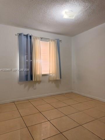 An empty room features beige tile flooring, white walls, and a window with layered curtains — 2400 NW 22nd Ct # 3, Miami FL 33142, MIAMI, FL