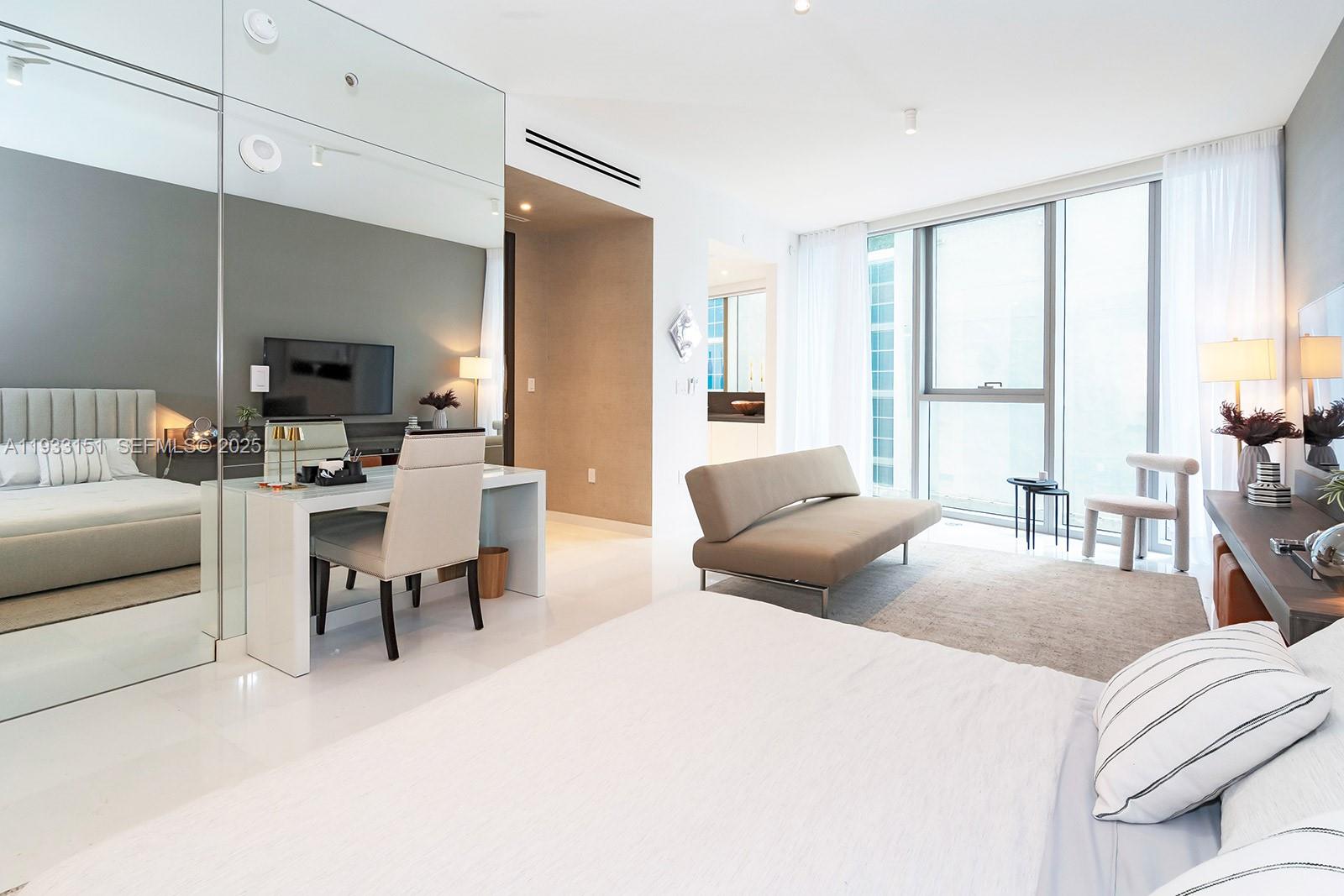 A modern bedroom features a bed, a desk, a sofa, and floor-to-ceiling windows — 300 Biscayne Blvd Way # 805, Miami FL 33131, MIAMI, FL