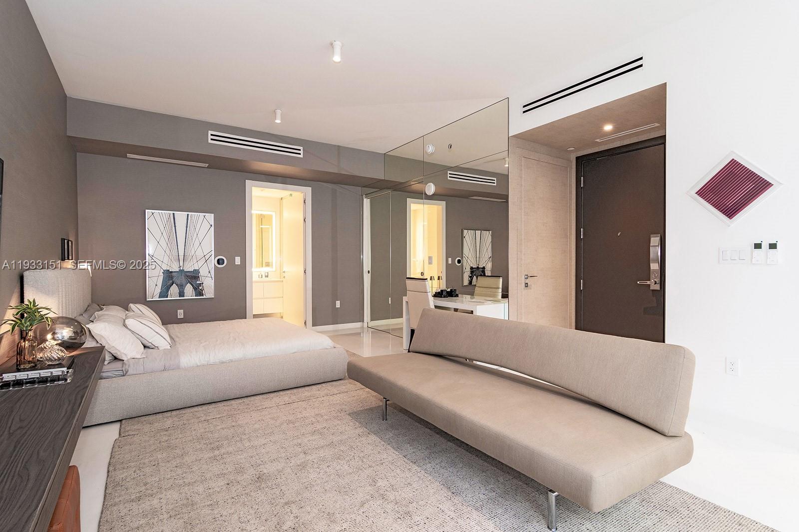 A modern bedroom features a low-profile bed, a sofa, and a mirrored wall — 300 Biscayne Blvd Way # 805, Miami FL 33131, MIAMI, FL