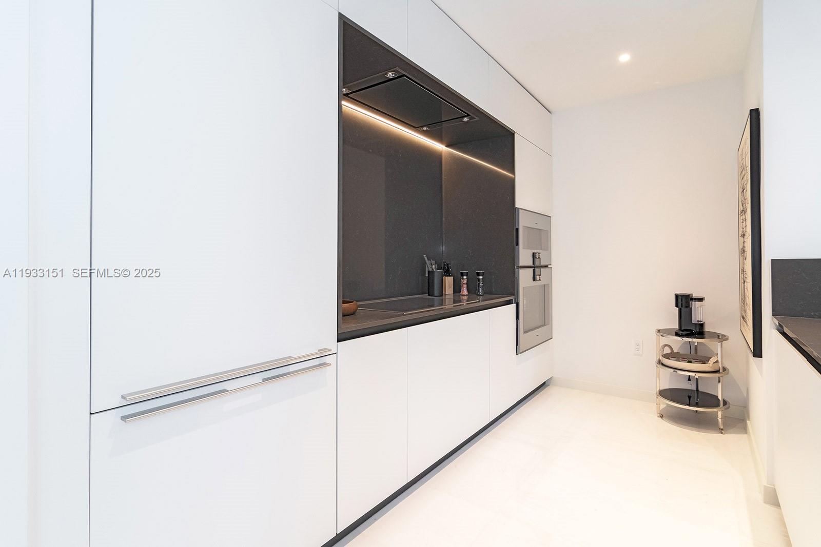 A modern kitchen features white cabinetry, a dark stone backsplash, and built-in stainless steel appliances — 300 Biscayne Blvd Way # 805, Miami FL 33131, MIAMI, FL