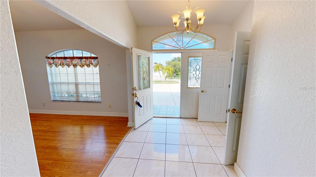 An entryway with white tile floors, a chandelier, and a view through the open front door — 2244 MAURITANIA ROAD, PUNTA GORDA, FL