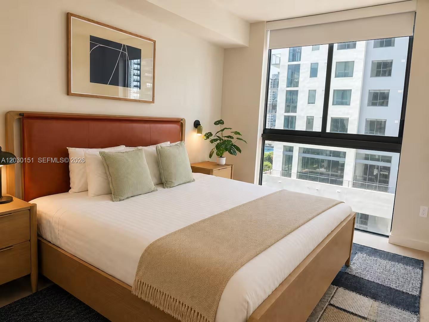 A bedroom features a leather headboard, a bed with neutral bedding, and a large window — 11 NE 6th St # 1212, Miami FL 33132, MIAMI, FL