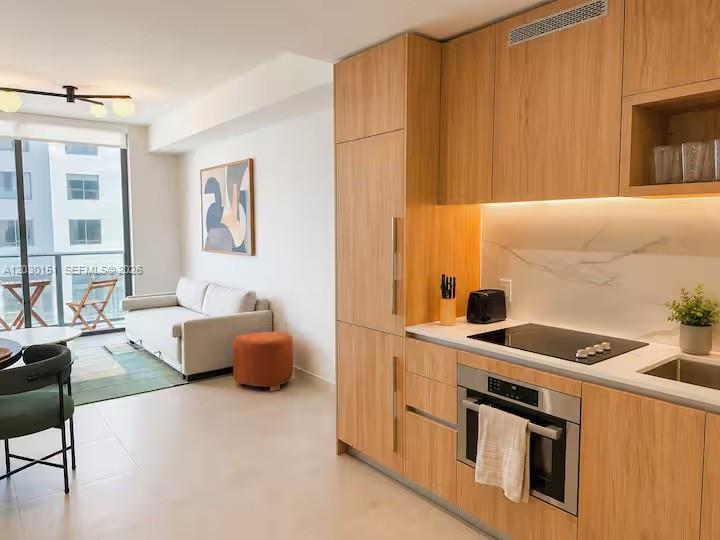 A modern kitchen with light wood cabinetry sits adjacent to a living area with balcony access — 11 NE 6th St # 1212, Miami FL 33132, MIAMI, FL