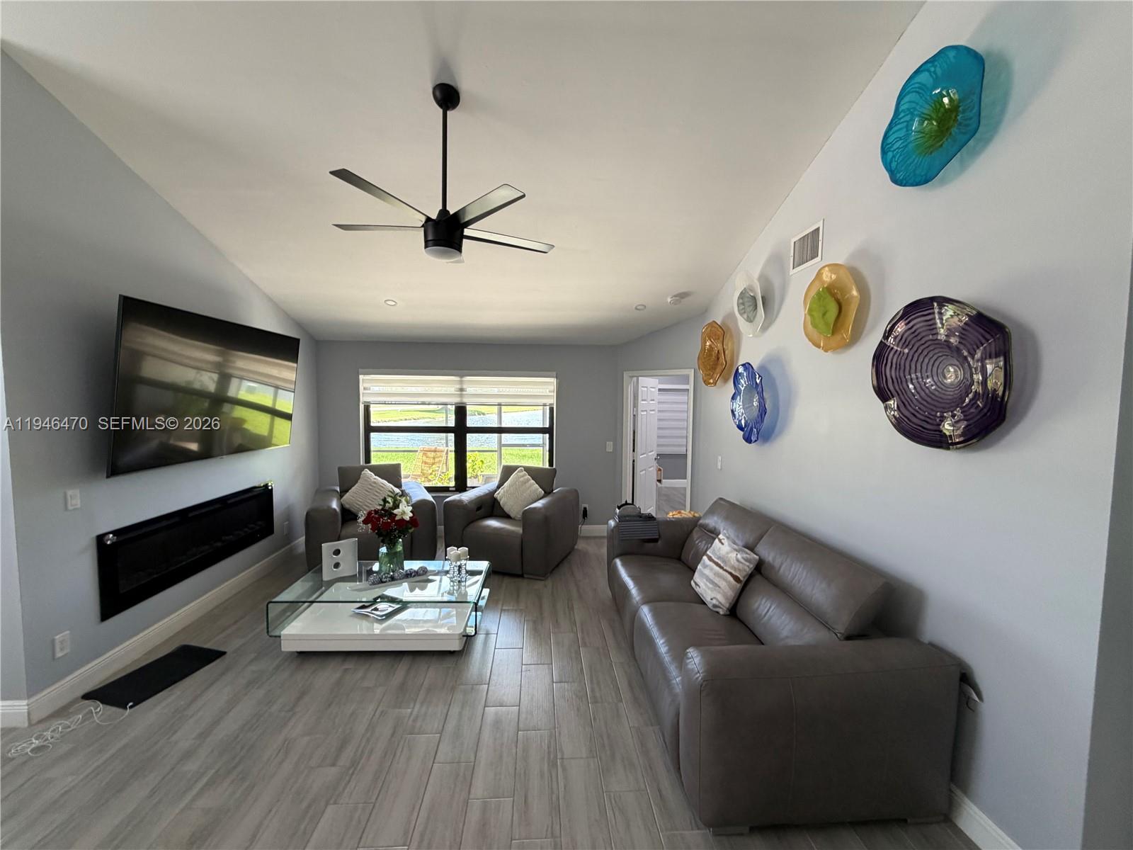 A living room features a fireplace, wall-mounted television, gray leather furniture, and decorative wall plates — 6788 Bitterbush Pl, Boynton Beach FL 33472, BOYNTON BEACH, FL