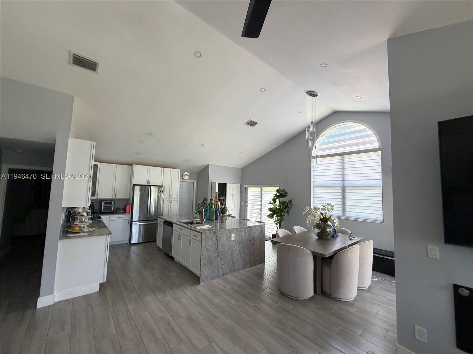 An open-concept kitchen and dining area features white cabinetry, a granite island, and vaulted ceilings — 6788 Bitterbush Pl, Boynton Beach FL 33472, BOYNTON BEACH, FL