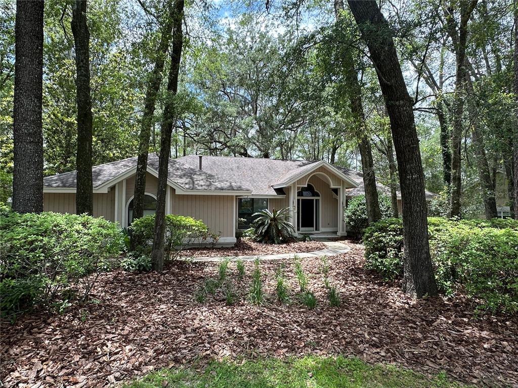 A single-story house with light-colored vertical siding is surrounded by trees and landscaping — 4722 SW 88TH DRIVE, GAINESVILLE, FL