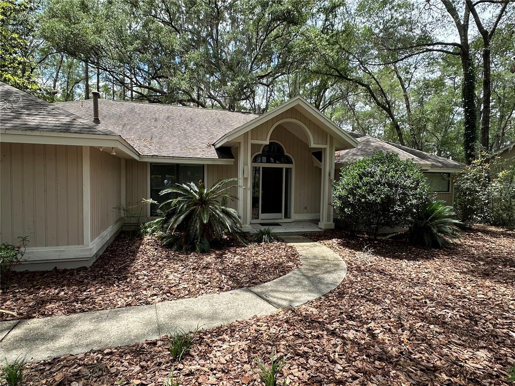 A tan house with vertical siding features a covered entryway and a curved concrete walkway — 4722 SW 88TH DRIVE, GAINESVILLE, FL