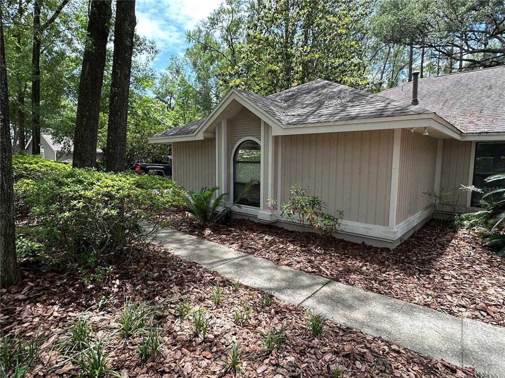 A beige house with vertical siding and an arched window sits beside a concrete walkway — 4722 SW 88TH DRIVE, GAINESVILLE, FL
