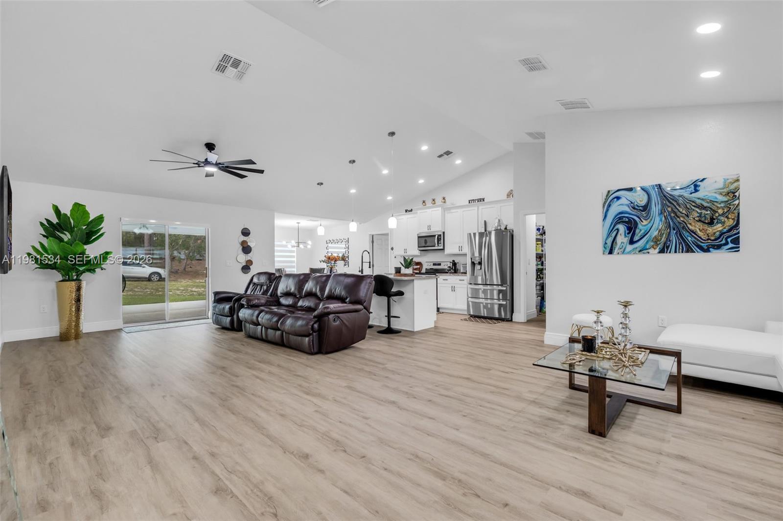 An open-concept living room and kitchen featuring light wood floors and white cabinetry — 13822 SW 61 Pl Rd, Ocala FL 34481, OCALA, FL