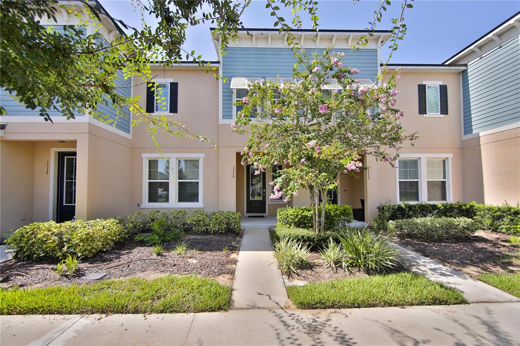 A multi-unit townhouse exterior features beige stucco, blue siding, and a central flowering tree — 1515 CAREY PALM CIRCLE, KISSIMMEE, FL