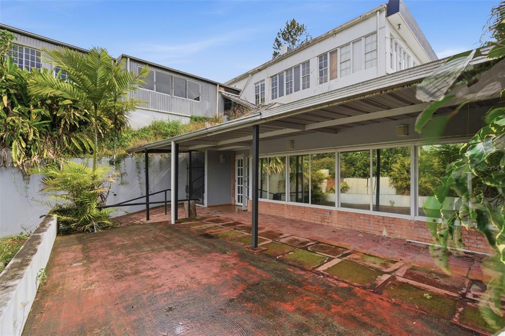 A covered patio with red tiled flooring sits beside a multi-story building with large windows — carr. 739, km. 3.4 CAMINO MONTICELLO, CIDRA, PR