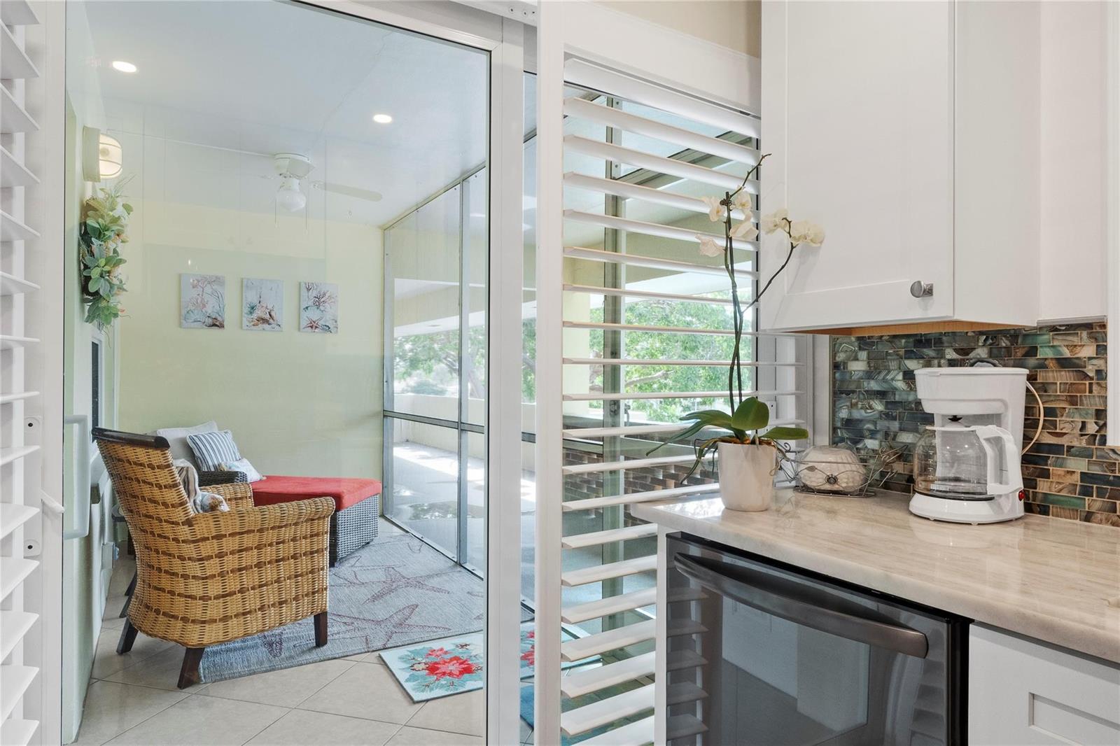 A kitchen with white cabinets and a coffee maker overlooks a screened-in balcony with seating — 1340 NE 28th Avenue # 242, Pompano Beach FL 33062, POMPANO BEACH, FL