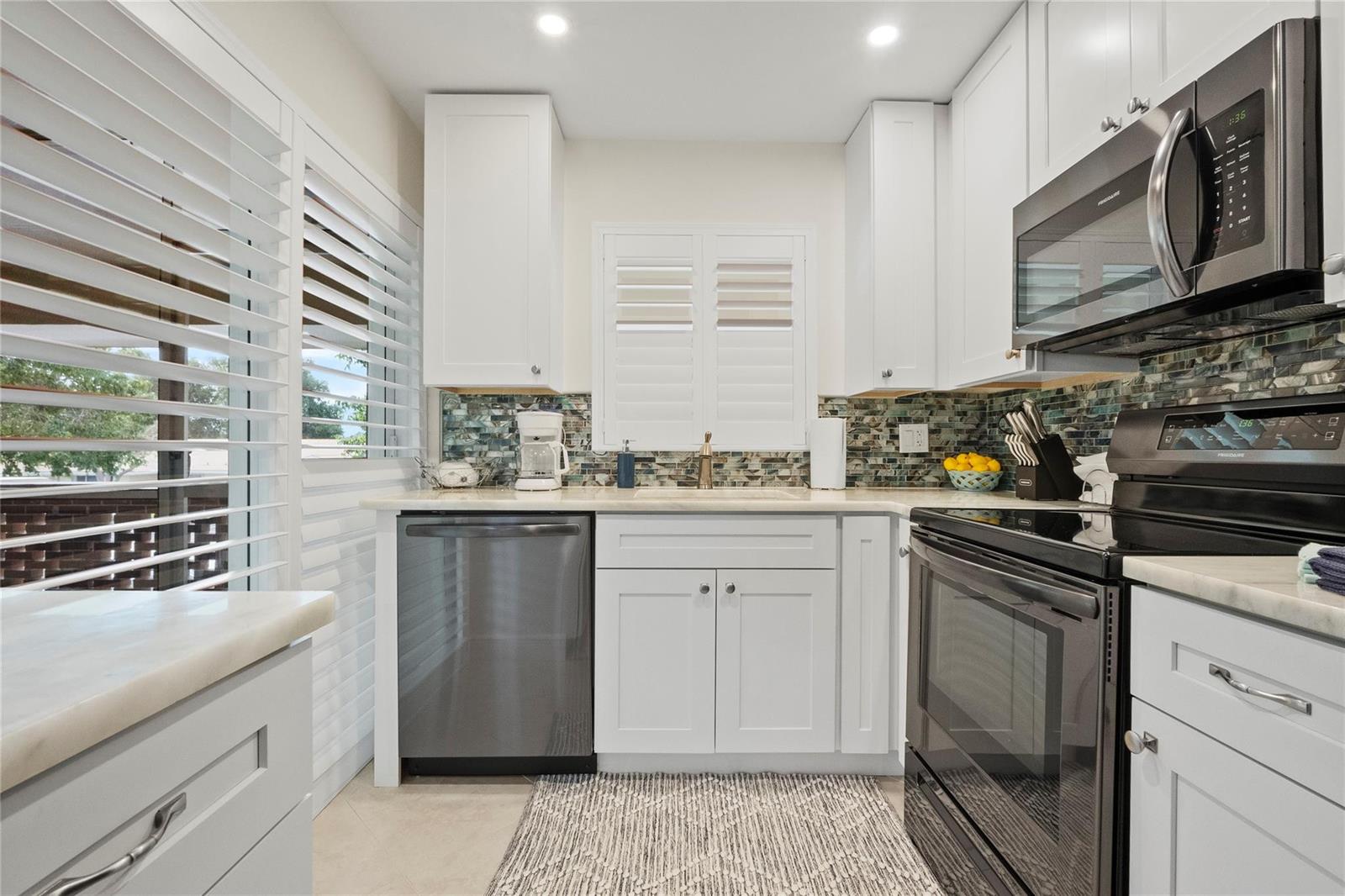 A kitchen features white cabinets, stainless steel appliances, a mosaic tile backsplash, and plantation shutters — 1340 NE 28th Avenue # 242, Pompano Beach FL 33062, POMPANO BEACH, FL