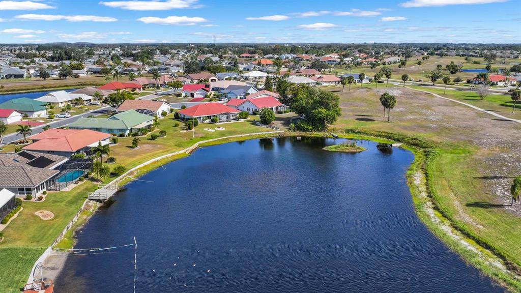 An aerial view shows a residential neighborhood with houses surrounding a large, central pond — 705 WESTMONT WAY, SUN CITY CENTER, FL