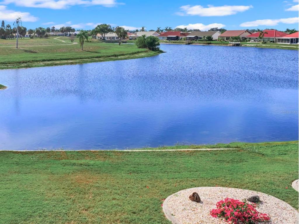 A view of a lake surrounded by grassy lawns and residential houses under a blue sky — 705 WESTMONT WAY, SUN CITY CENTER, FL