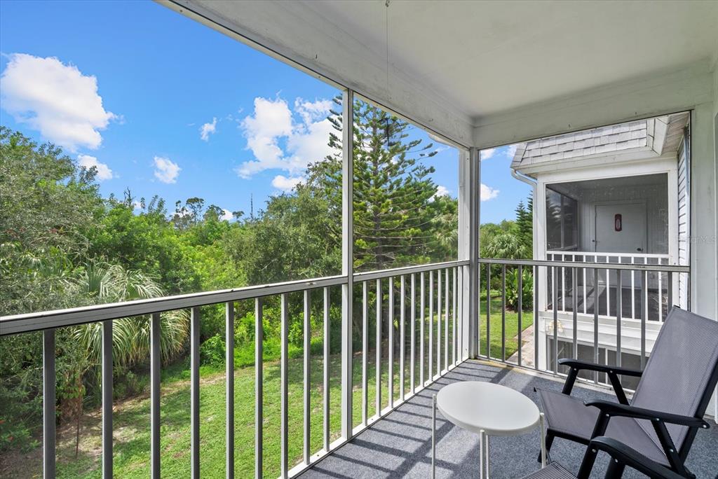 A screened-in balcony features a white railing, a small table, and a chair overlooking trees — 22375 EDGEWATER DRIVE UNIT 241, PORT CHARLOTTE, FL