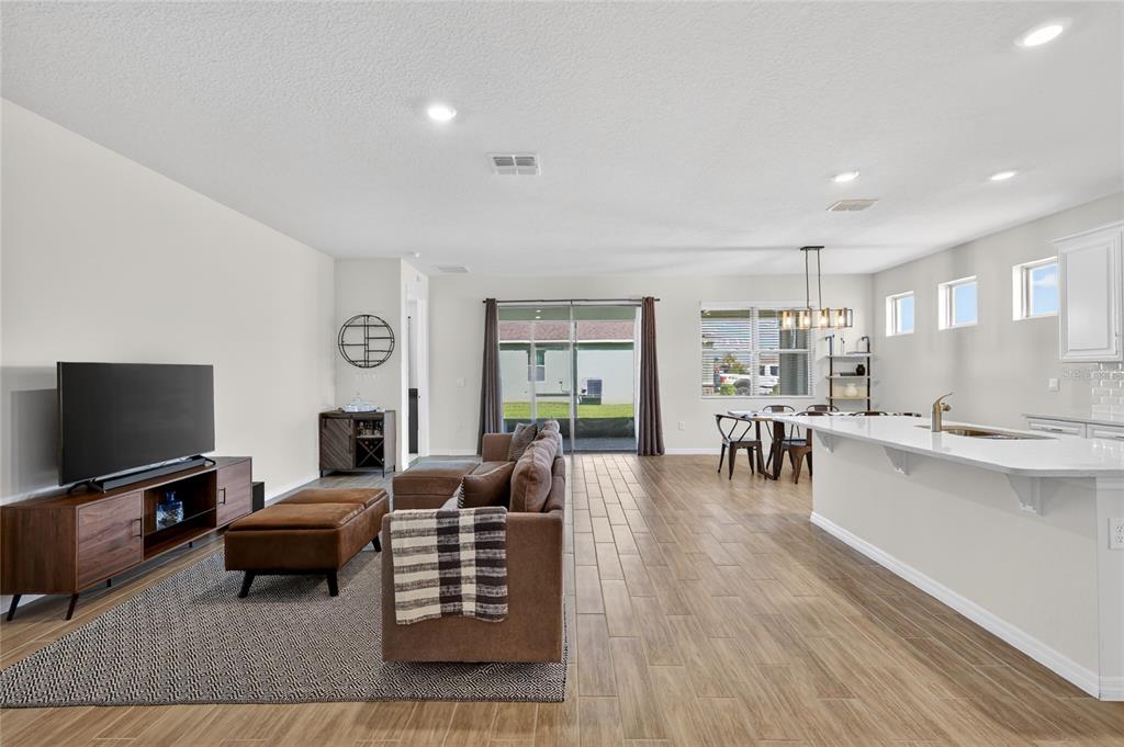 An open-concept living room and kitchen featuring wood-look tile flooring and a sliding glass door — 1558 TISBURY PT, SANFORD, FL