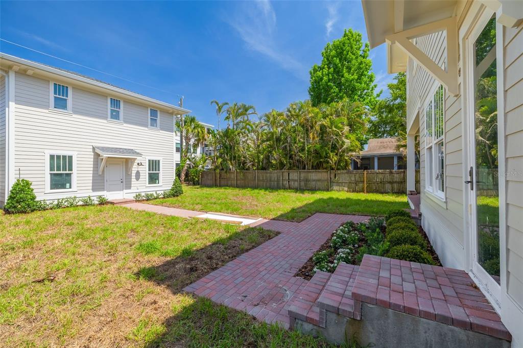 A backyard with a brick patio, a grassy lawn, and two light-colored multi-story houses — 2011 10TH STREET N, ST PETERSBURG, FL