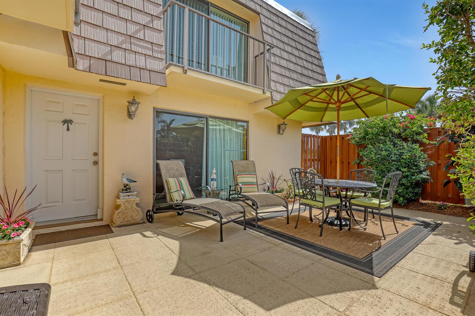 A patio features a dining set with a green umbrella, two lounge chairs, and a door — 131 Ocean Cove Drive, Jupiter FL 33477, JUPITER, FL