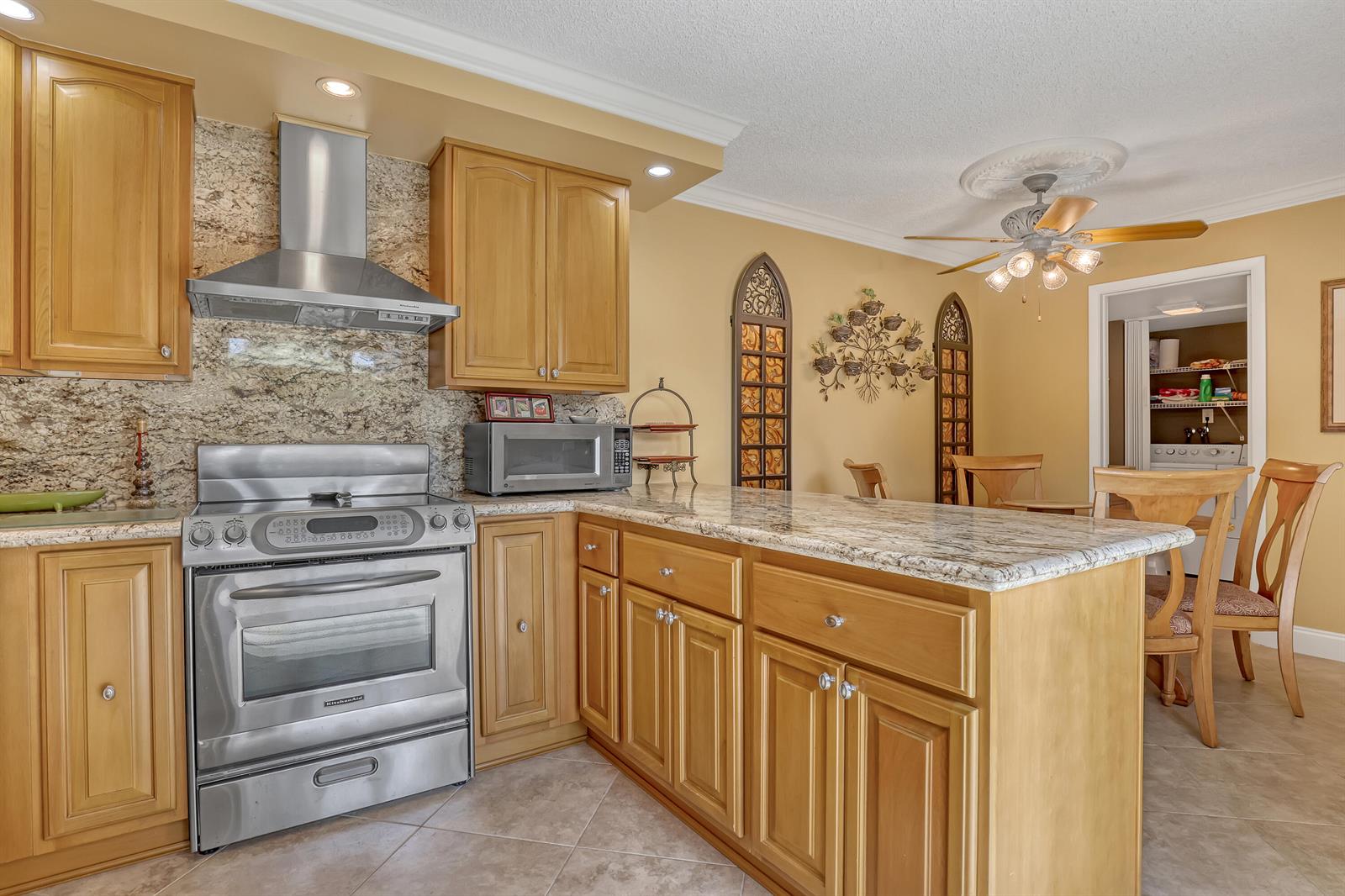 A kitchen with wood cabinets, granite countertops, stainless steel appliances, and a dining area — 131 Ocean Cove Drive, Jupiter FL 33477, JUPITER, FL