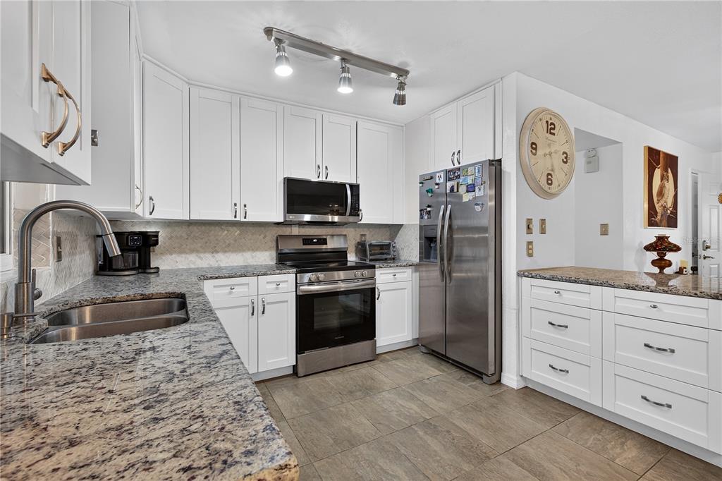 A kitchen features white cabinets, granite countertops, stainless steel appliances, and a large wall clock — 5010 STOLLS AVENUE, TAMPA, FL