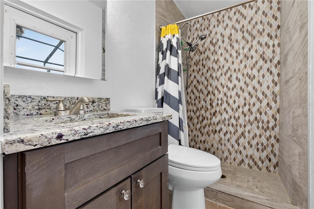 A bathroom features a dark wood vanity, granite countertop, toilet, and a tiled walk-in shower — 5010 STOLLS AVENUE, TAMPA, FL