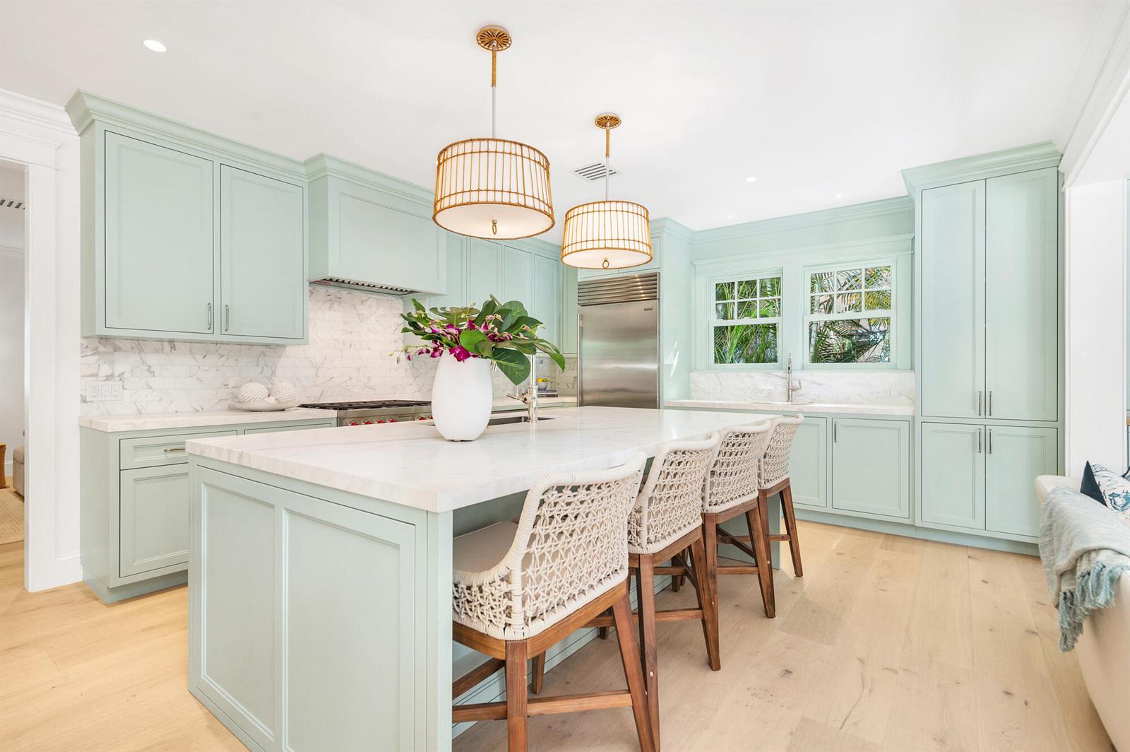 A kitchen with light green cabinets, a marble-topped island, and woven bar stools — 142 Seabreeze Avenue, Palm Beach FL 33480, PALM BEACH, FL