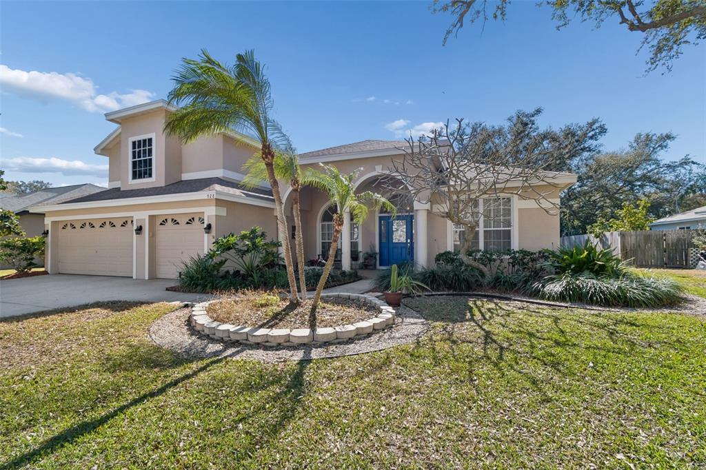 A tan single-story house with a blue front door and a circular stone garden bed — 928 OAKVIEW ROAD, TARPON SPRINGS, FL