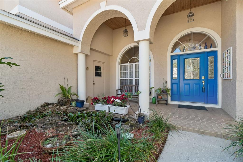 A covered entryway features a blue front door, a small pond, and a brick porch — 928 OAKVIEW ROAD, TARPON SPRINGS, FL