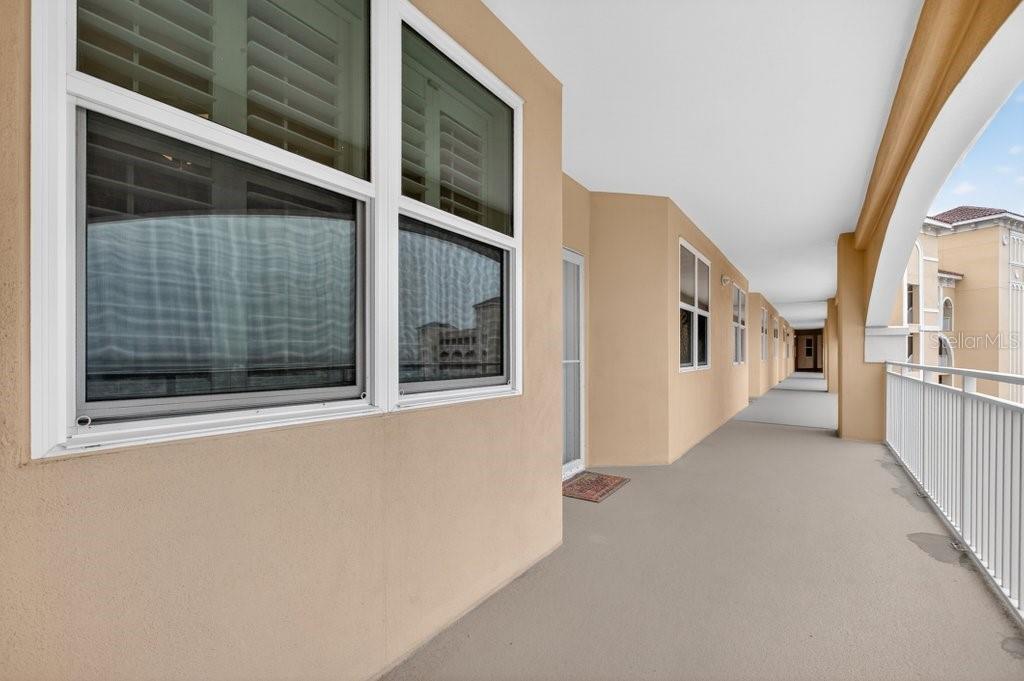 A long, covered outdoor balcony with beige walls, white railings, and multiple windows — 80 SURFVIEW DRIVE UNIT 707, PALM COAST, FL