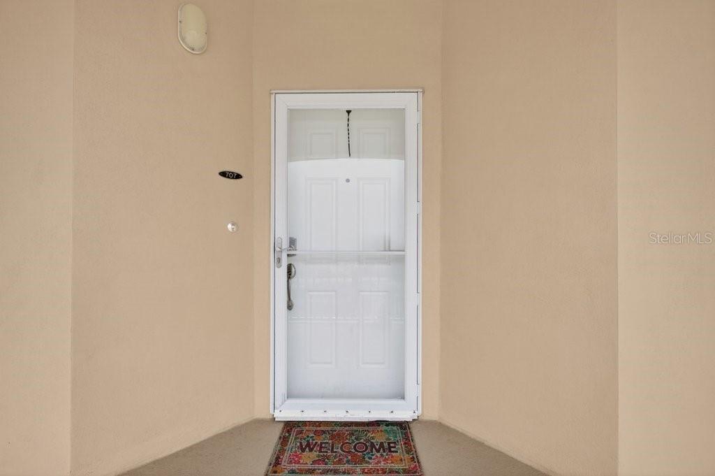 A white storm door with a welcome mat sits on a beige exterior entryway — 80 SURFVIEW DRIVE UNIT 707, PALM COAST, FL