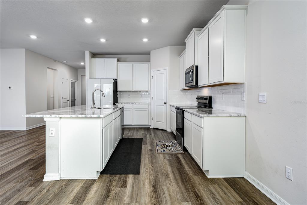 A kitchen with white cabinets, marble-look countertops, a center island, and wood-style flooring — 10622 EUSTIS DRIVE, PARRISH, FL