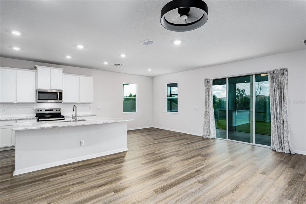 A modern kitchen with white cabinets and a marble island opens to a living area — 10622 EUSTIS DRIVE, PARRISH, FL