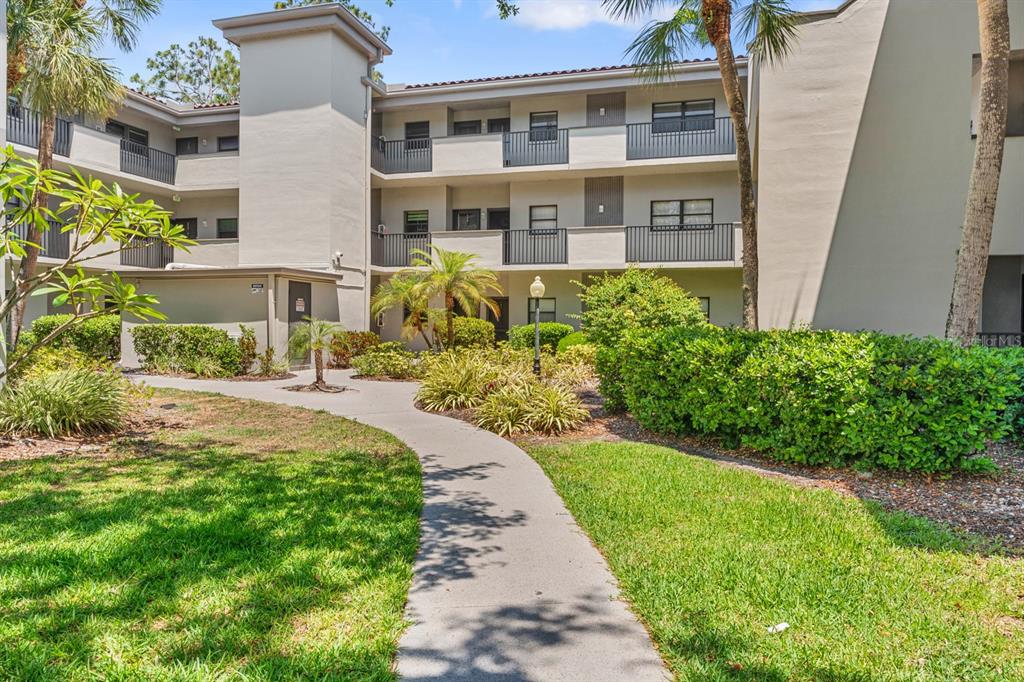 A concrete walkway leads to the entrance of a three-story apartment building with balconies — 2650 COUNTRYSIDE BOULEVARD UNIT B307, CLEARWATER, FL