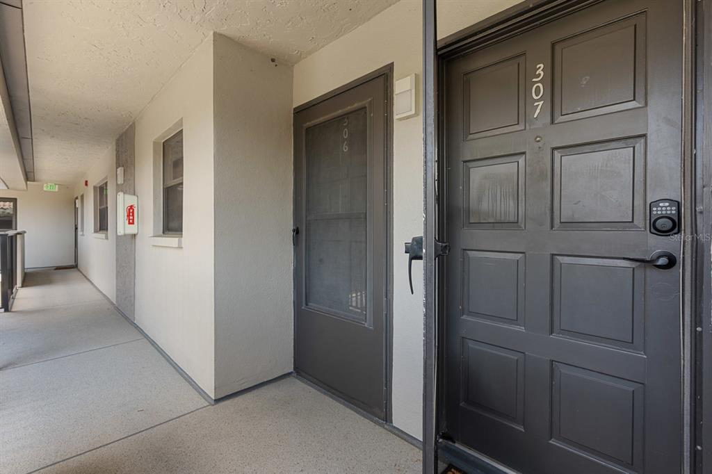 An exterior apartment hallway features two dark brown doors numbered 306 and 307 — 2650 COUNTRYSIDE BOULEVARD UNIT B307, CLEARWATER, FL