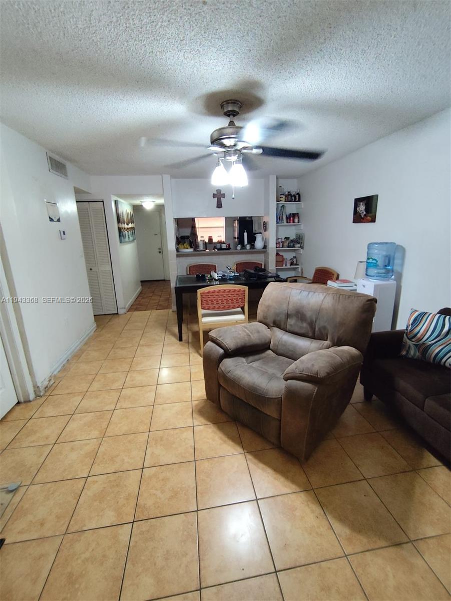 A living room with tile flooring, a brown recliner, and a dining area in the background — 19781 SW 114th Ave # 142, Miami FL 33157, MIAMI, FL