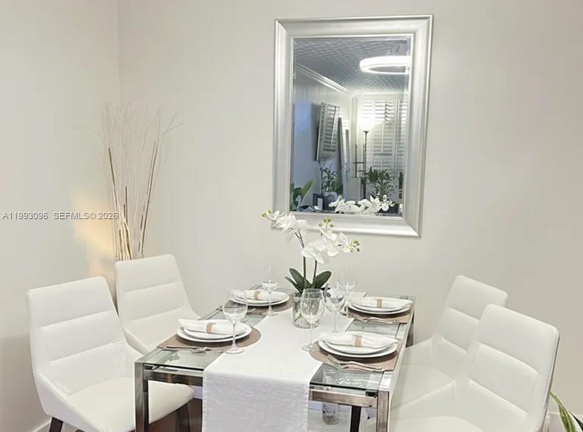 A dining room features a glass-topped table with four white chairs and a wall mirror — 2450 NE 135th St # 103, North Miami FL 33181, NORTH MIAMI, FL