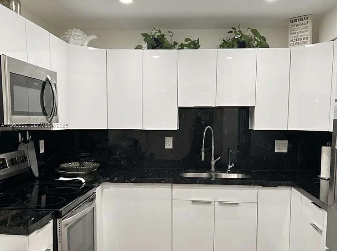 A kitchen features white flat-panel cabinets, a black countertop, and a black backsplash — 2450 NE 135th St # 103, North Miami FL 33181, NORTH MIAMI, FL