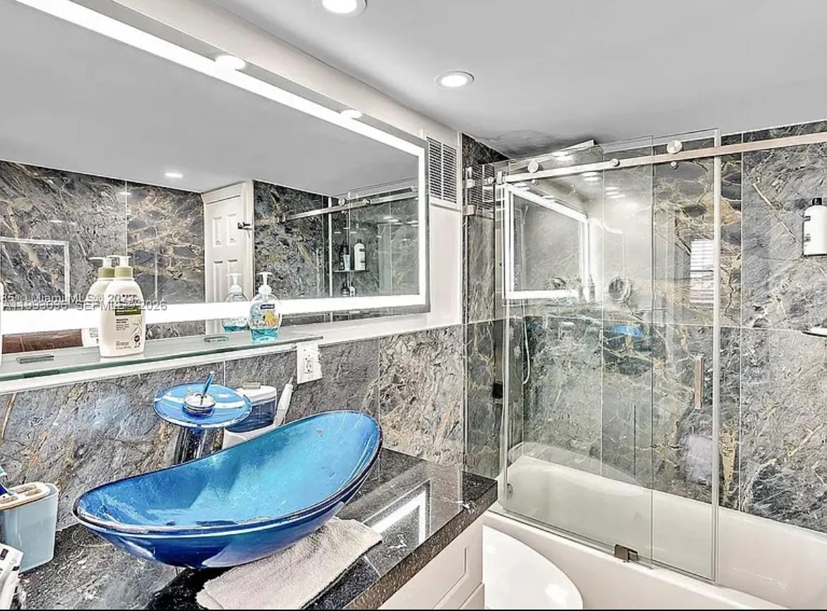 A bathroom features a blue vessel sink, dark marble walls, and a glass-enclosed shower — 2450 NE 135th St # 103, North Miami FL 33181, NORTH MIAMI, FL