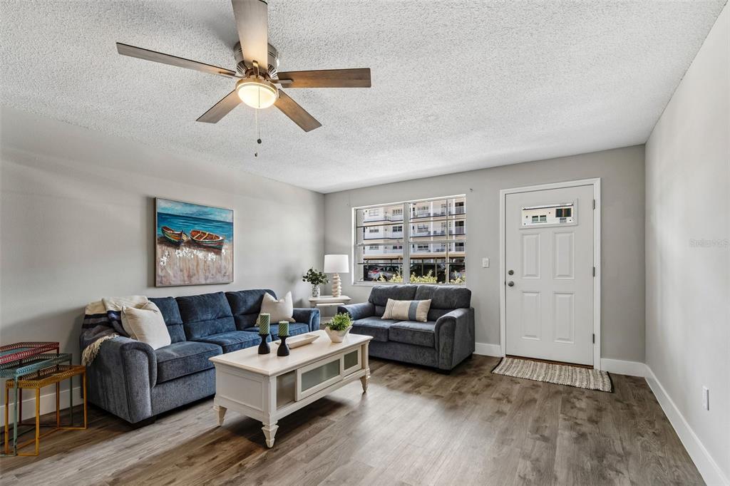 A living room features a blue sofa and loveseat, a coffee table, and wood flooring — 5955 30TH AVENUE S UNIT 105, GULFPORT, FL