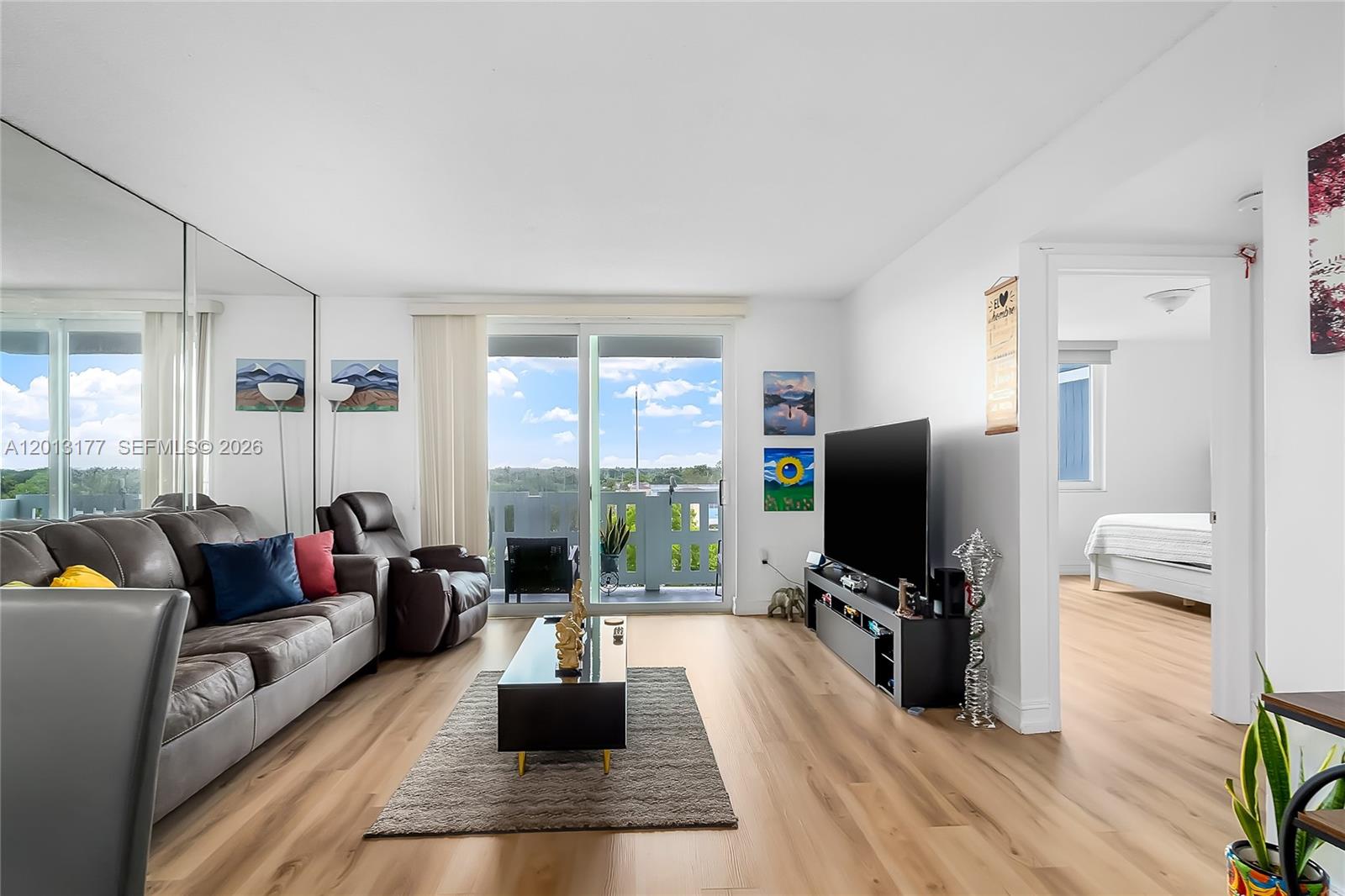 A living room features light wood flooring, a grey sofa, a television, and a balcony view — 919 Hillcrest Dr # 607, Hollywood FL 33021, HOLLYWOOD, FL