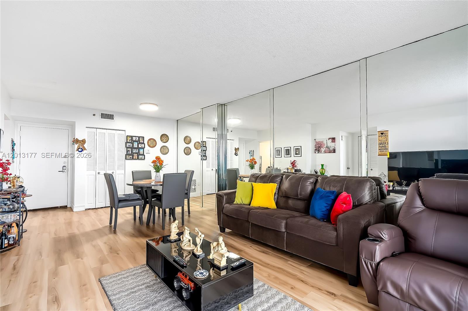 A living room features a brown leather sofa, mirrored wall, and light wood flooring — 919 Hillcrest Dr # 607, Hollywood FL 33021, HOLLYWOOD, FL