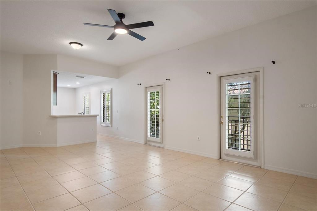 A bright living room features light tile flooring, a ceiling fan, and two glass doors — 1007 CELEBRATION AVENUE UNIT 201, CELEBRATION, FL
