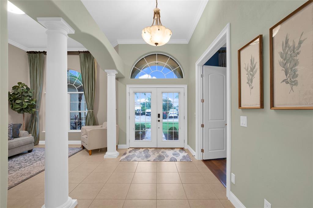 A tiled entryway features white columns, a chandelier, and double glass doors with a transom window — 3544 TUSCANY RESERVE BOULEVARD, NEW SMYRNA BEACH, FL