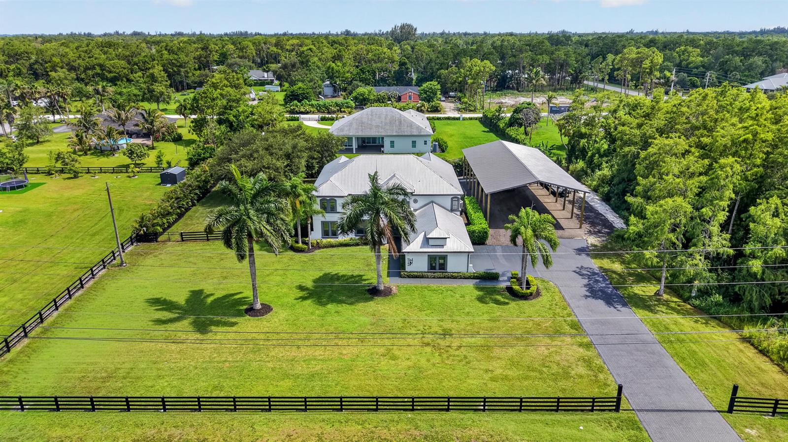 An aerial view shows a white house with a metal roof, palm trees, and carport — 17394 Orange Boulevard, FL 33470, FL