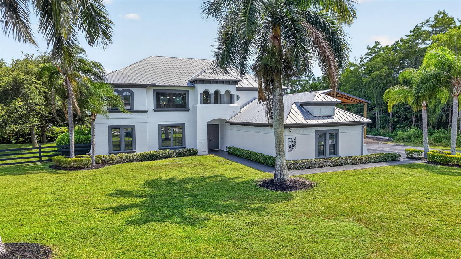 A two-story white house with a metal roof and dark trim sits on a grassy lawn — 17394 Orange Boulevard, FL 33470, FL